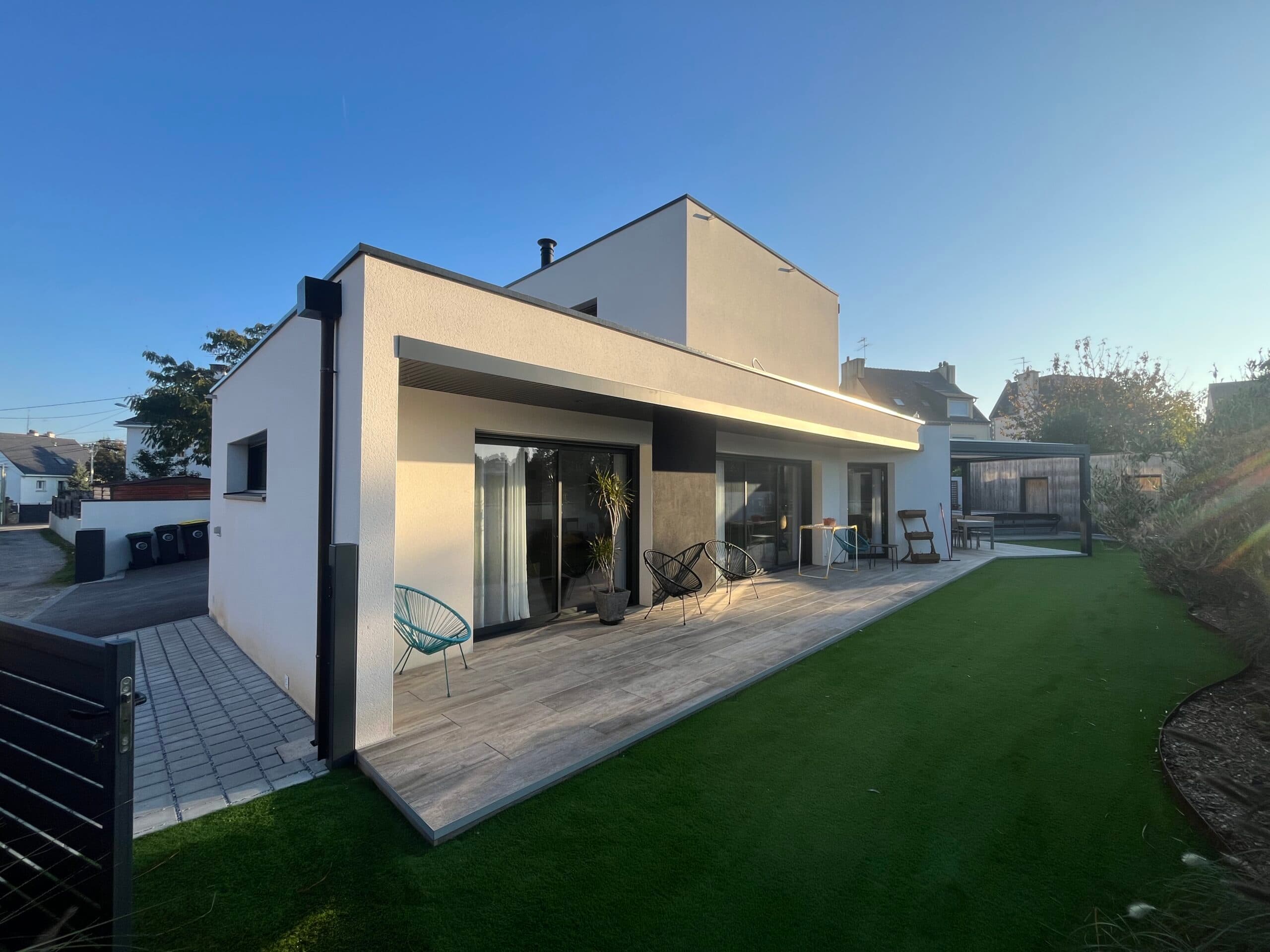 Maison contemporaine avec grande terrasse carrelée et pelouse synthétique, construction neuve réalisée par AJY Maçonnerie dans le Morbihan.