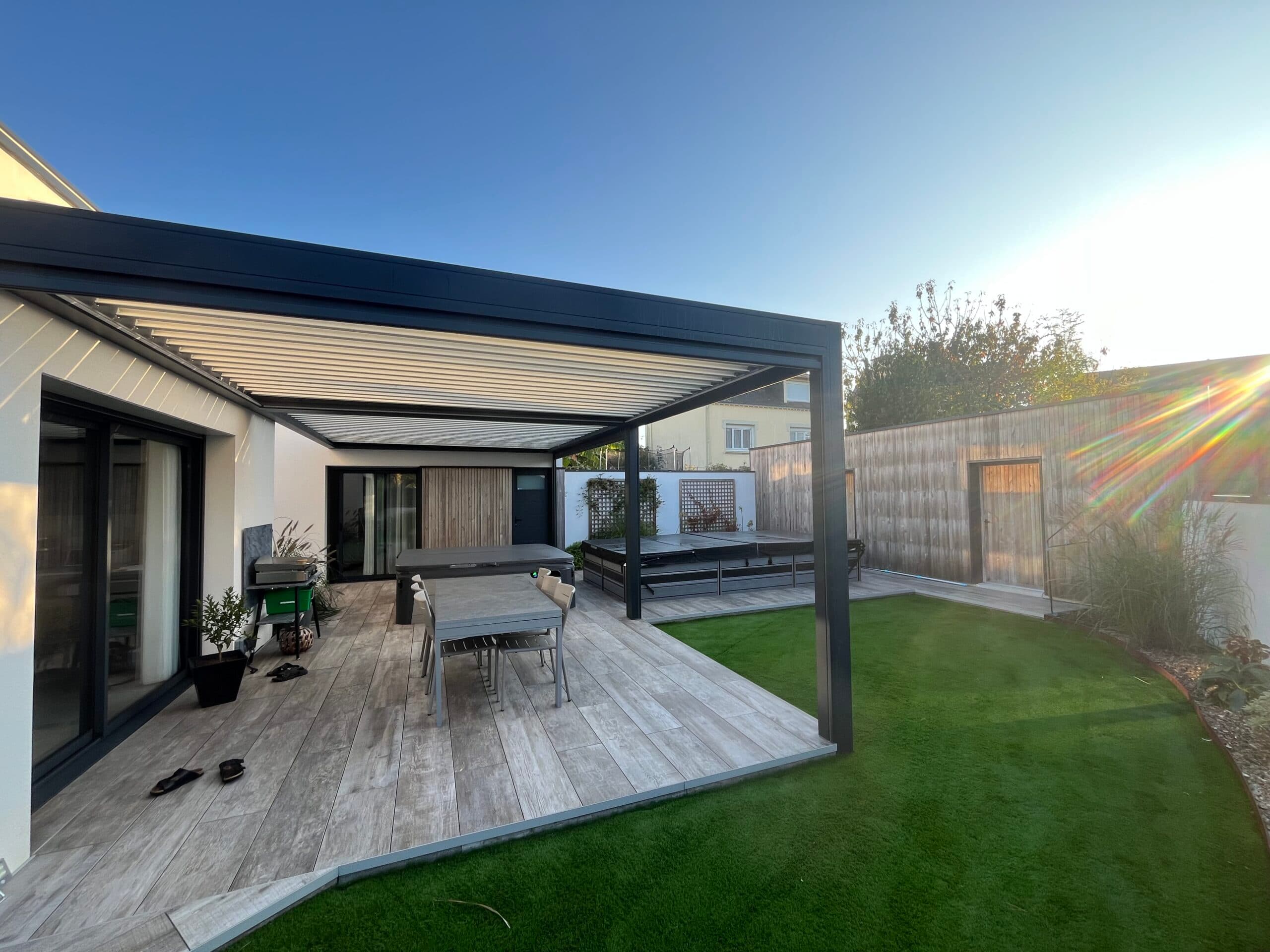 Terrasse moderne en carrelage effet bois avec pergola bioclimatique et spa, aménagement extérieur réalisé par AJY Maçonnerie dans le Morbihan.