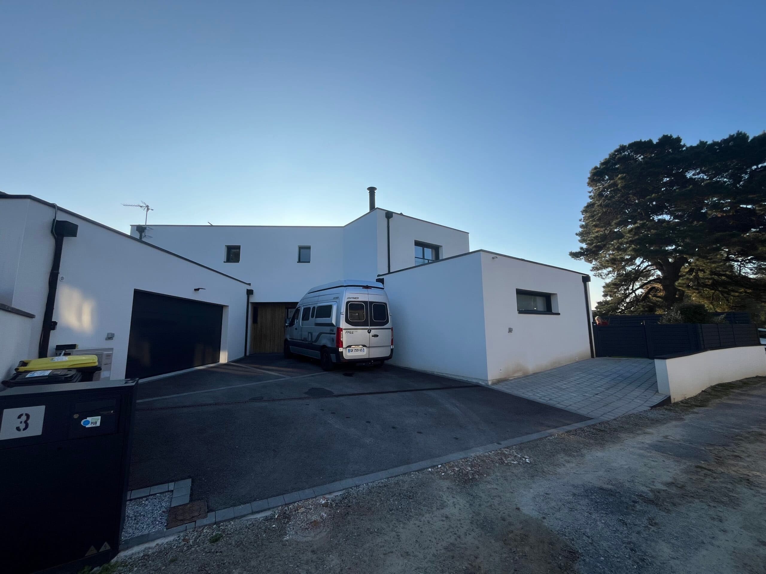 Façade avant de maison contemporaine blanche avec garage double et cour en enrobé réalisée par AJY Maçonnerie
