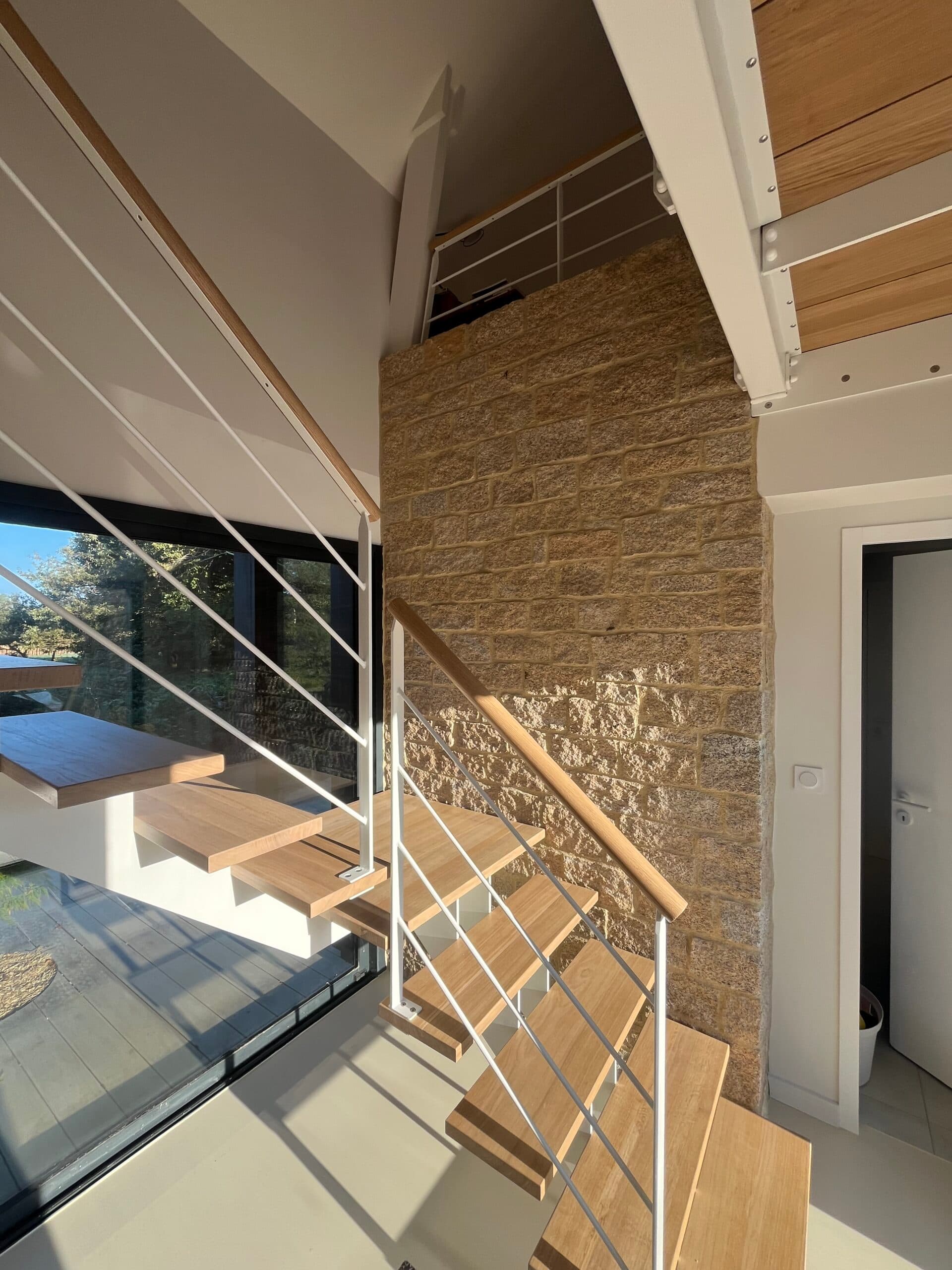 Vue de loin d’une maison moderne AJY Maçonnerie avec garage double, enduit blanc et terrain paysager dans un lotissement récent.