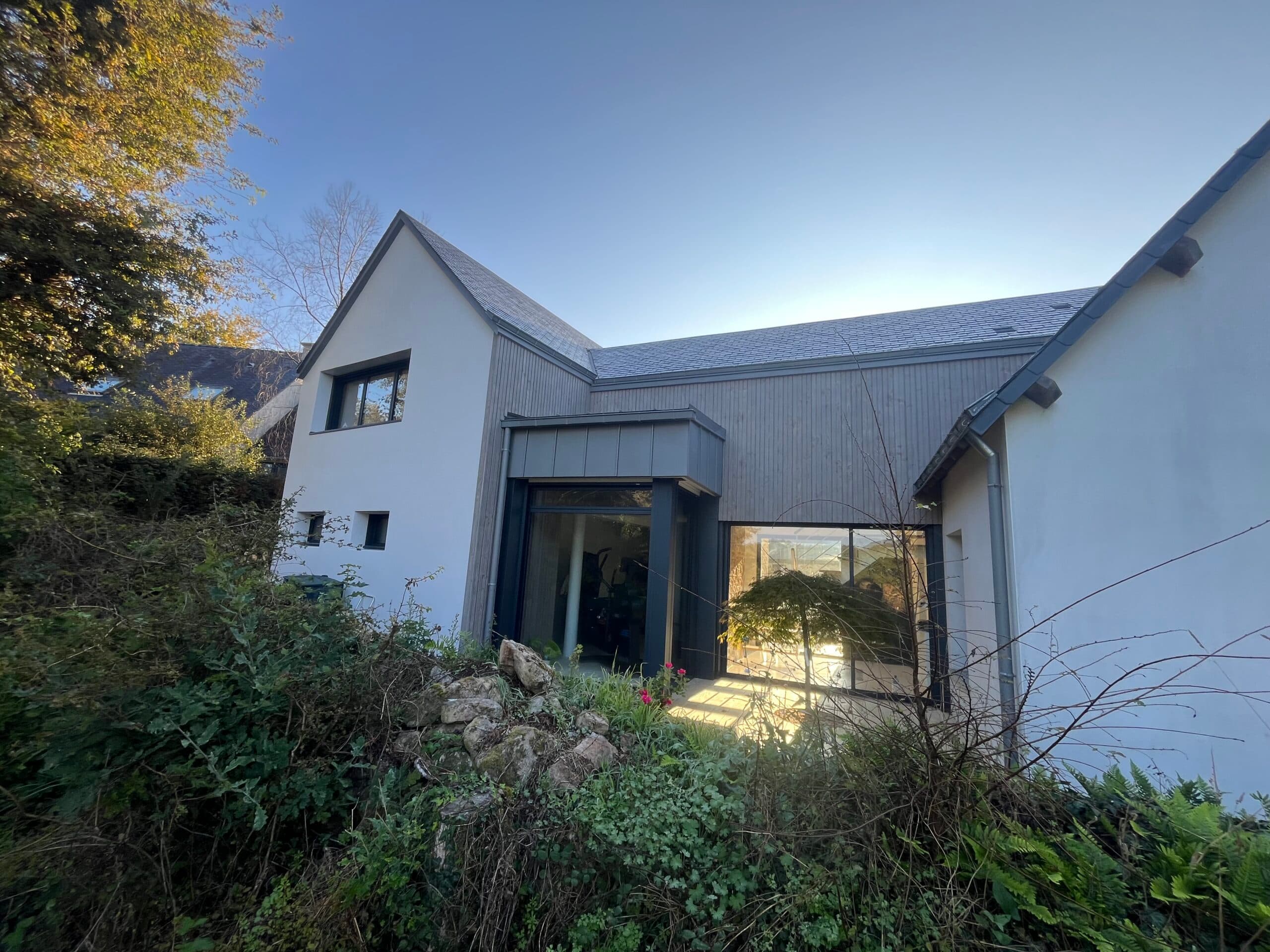 Façade principale d’une maison rénovée par AJY Maçonnerie, associant bâti ancien, extension bois et parement pierre autour du garage.