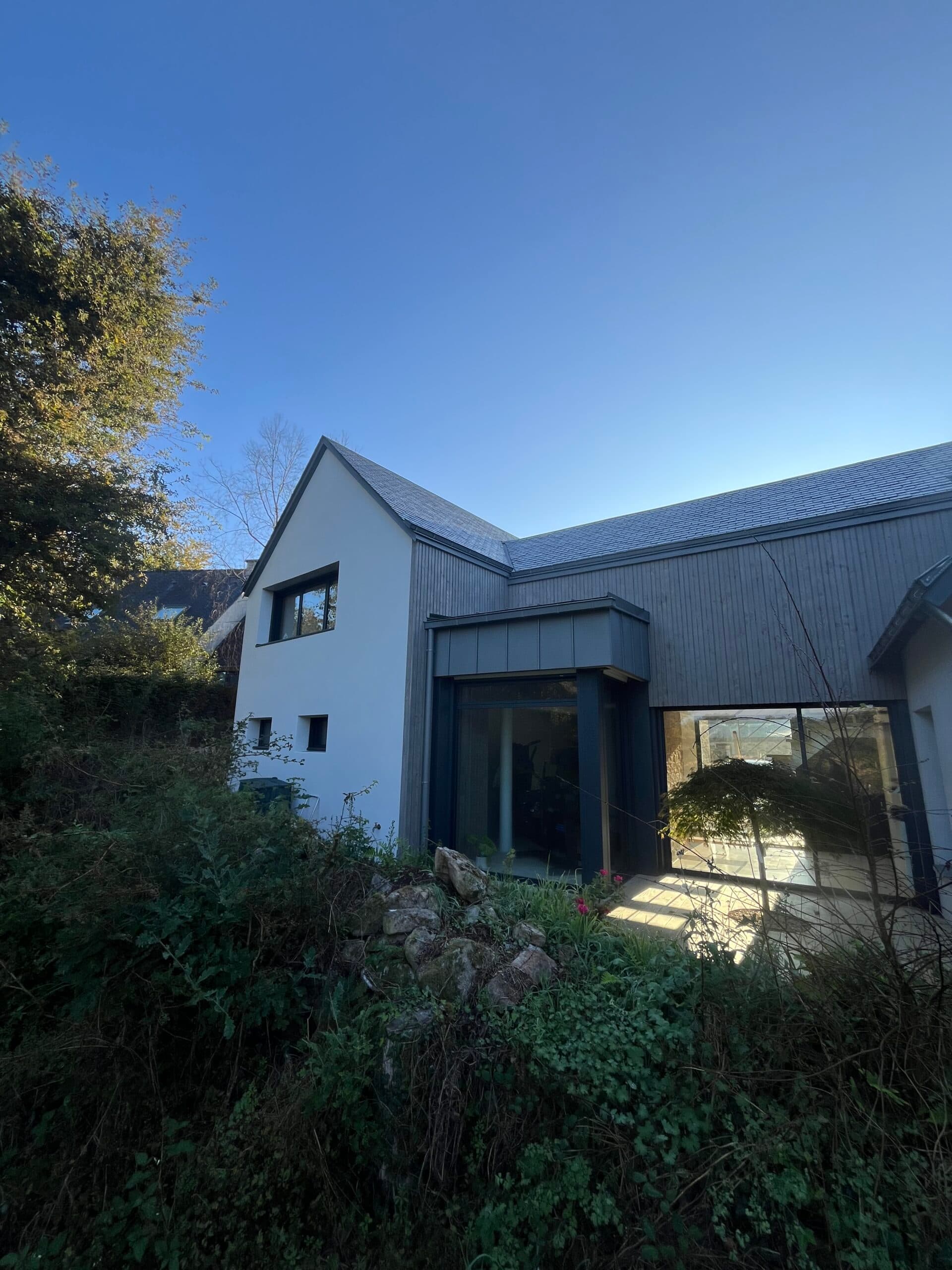Détail de l’extension en bardage bois et pierre naturelle réalisée par AJY Maçonnerie avec grande baie vitrée sur escalier intérieur.