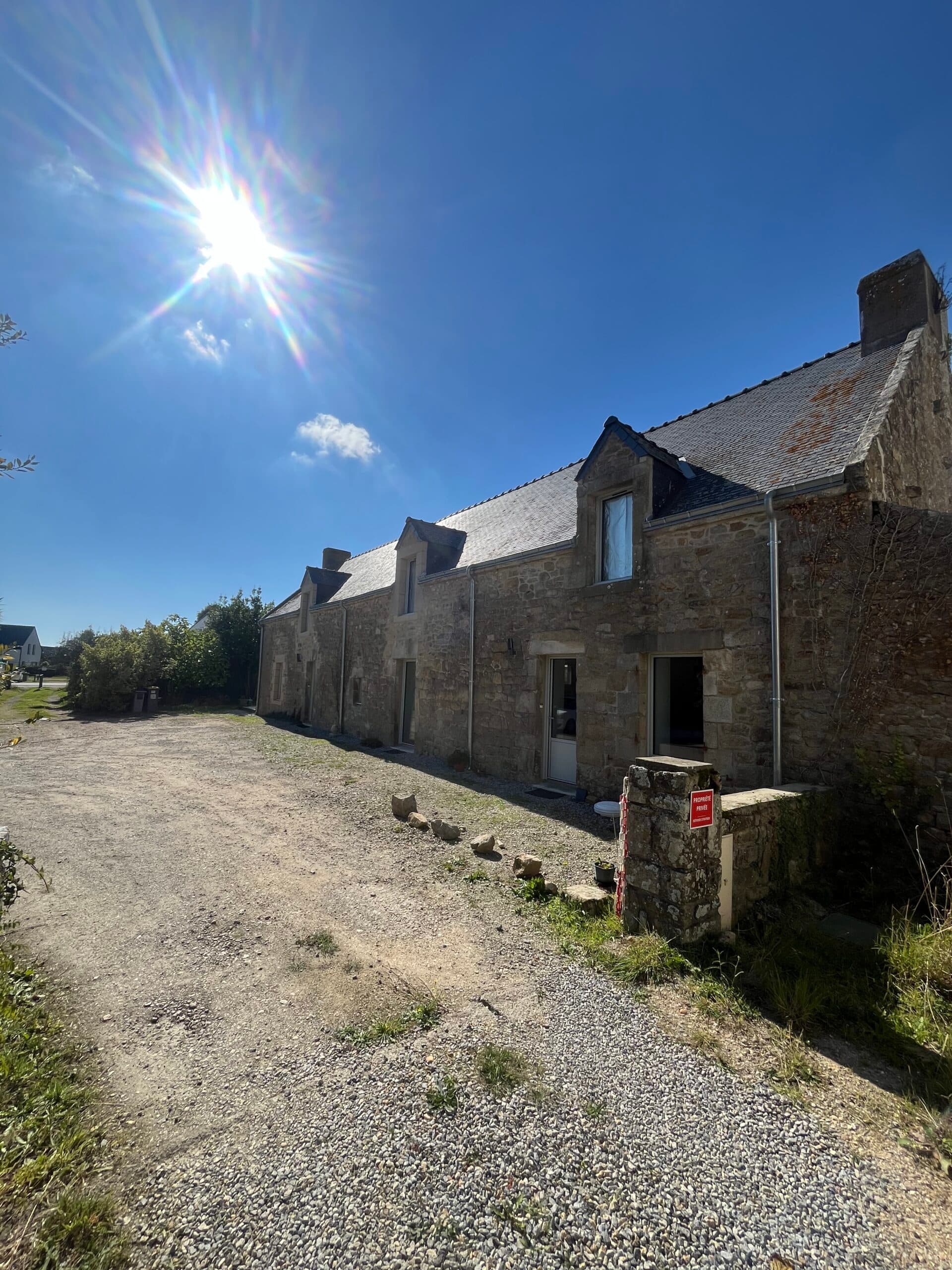 Chantier AJY Maçonnerie en bord de mer avec façade en pierre, mur et piliers de portail en granit et engin de terrassement préparant les aménagements extérieurs.