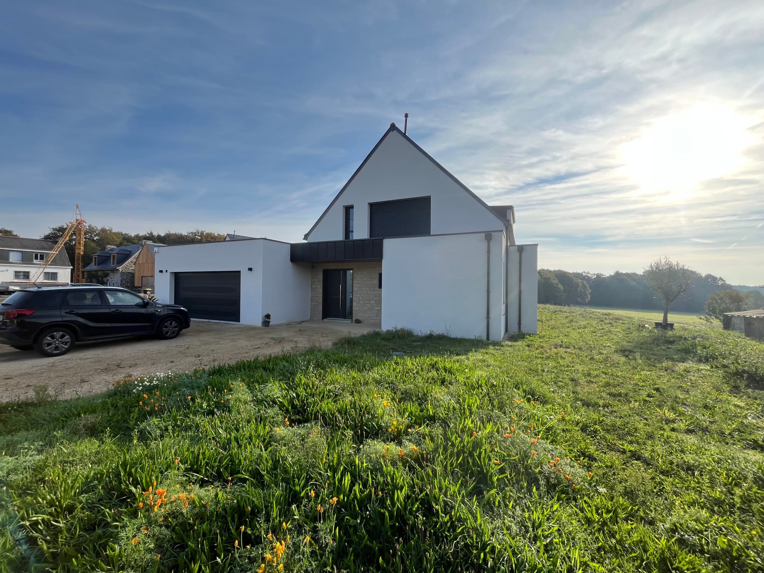 Construction de maison contemporaine AJY Maçonnerie avec enduit blanc, toiture ardoise et terrain paysager en campagne bretonne.