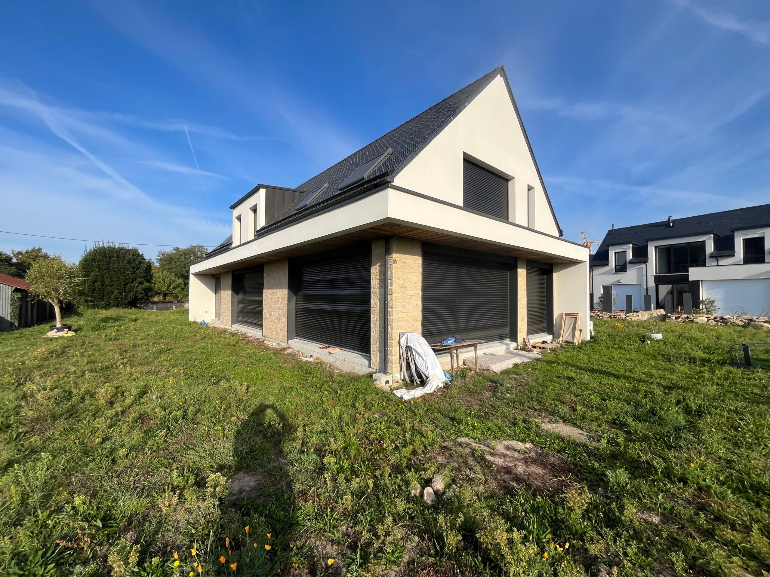 Vue avant d’une maison neuve AJY Maçonnerie avec garage attenant, enduit blanc et environnement verdoyant.