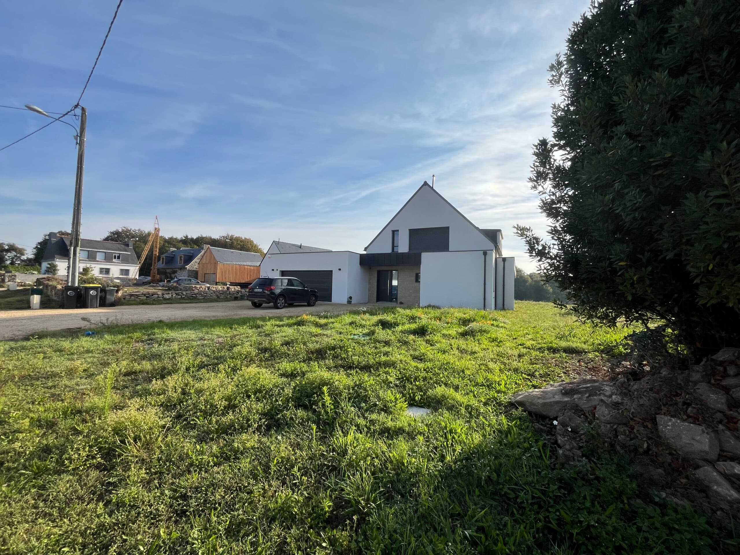 Maison contemporaine avec bardage bois, garage intégré et clôture en pierre, extension réalisée par AJY Maçonnerie.