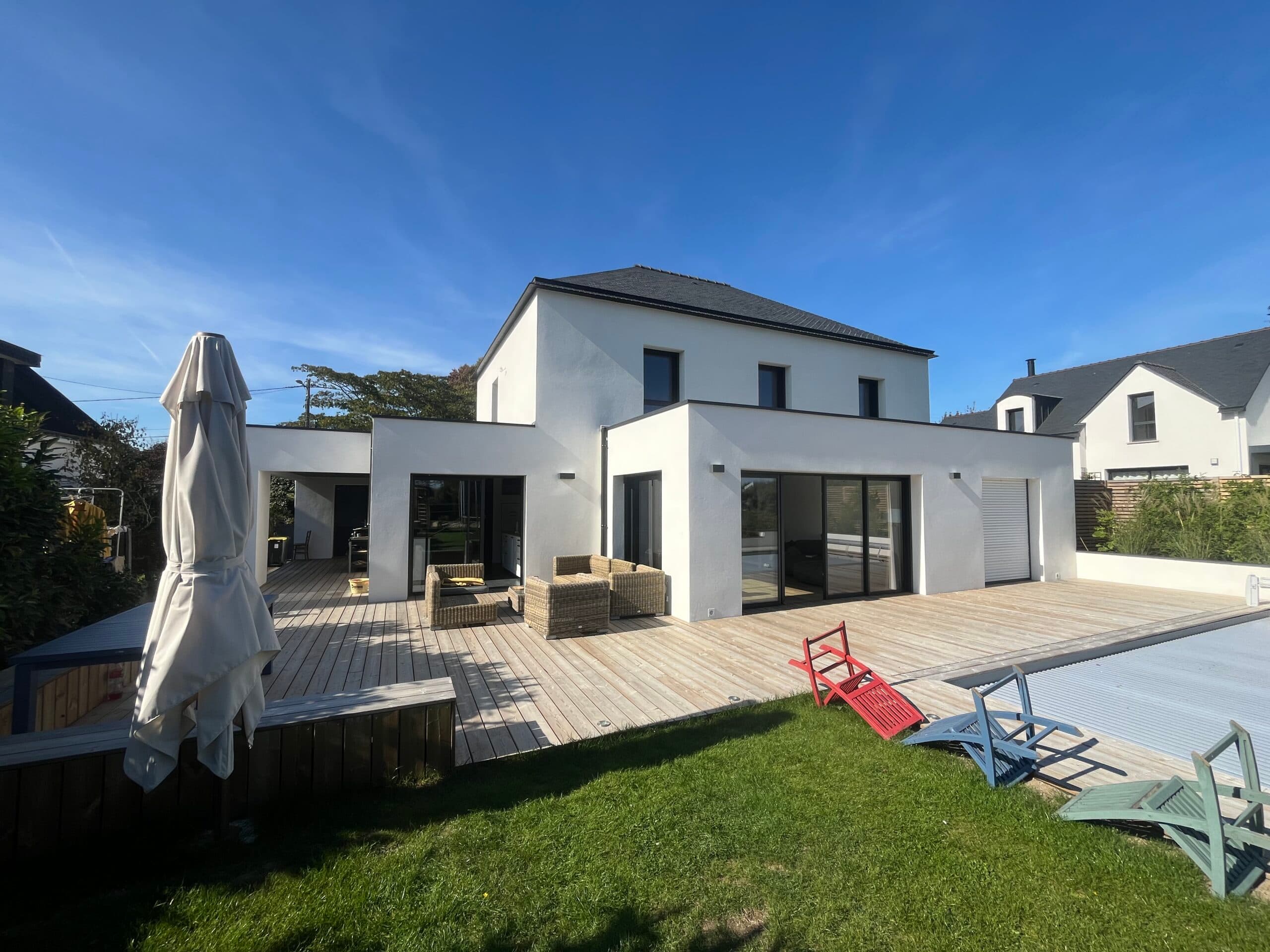 Maison contemporaine blanche avec grande piscine rectangulaire couverte et terrasse en bois dans un jardin paysagé en Bretagne