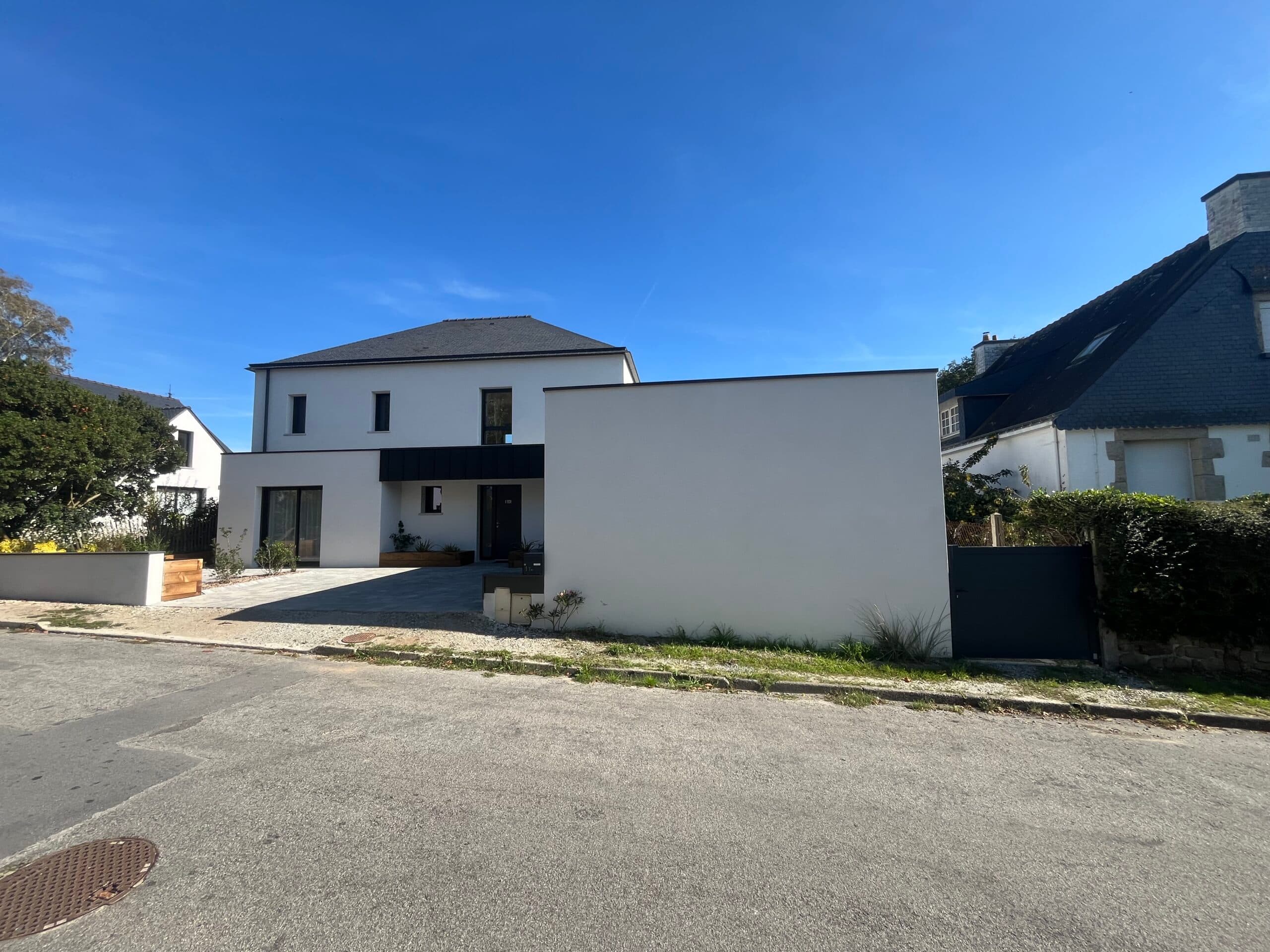 Façade de maison familiale moderne crépie blanc avec cour avant, garage attenant et végétation sur rue calme en bord de mer