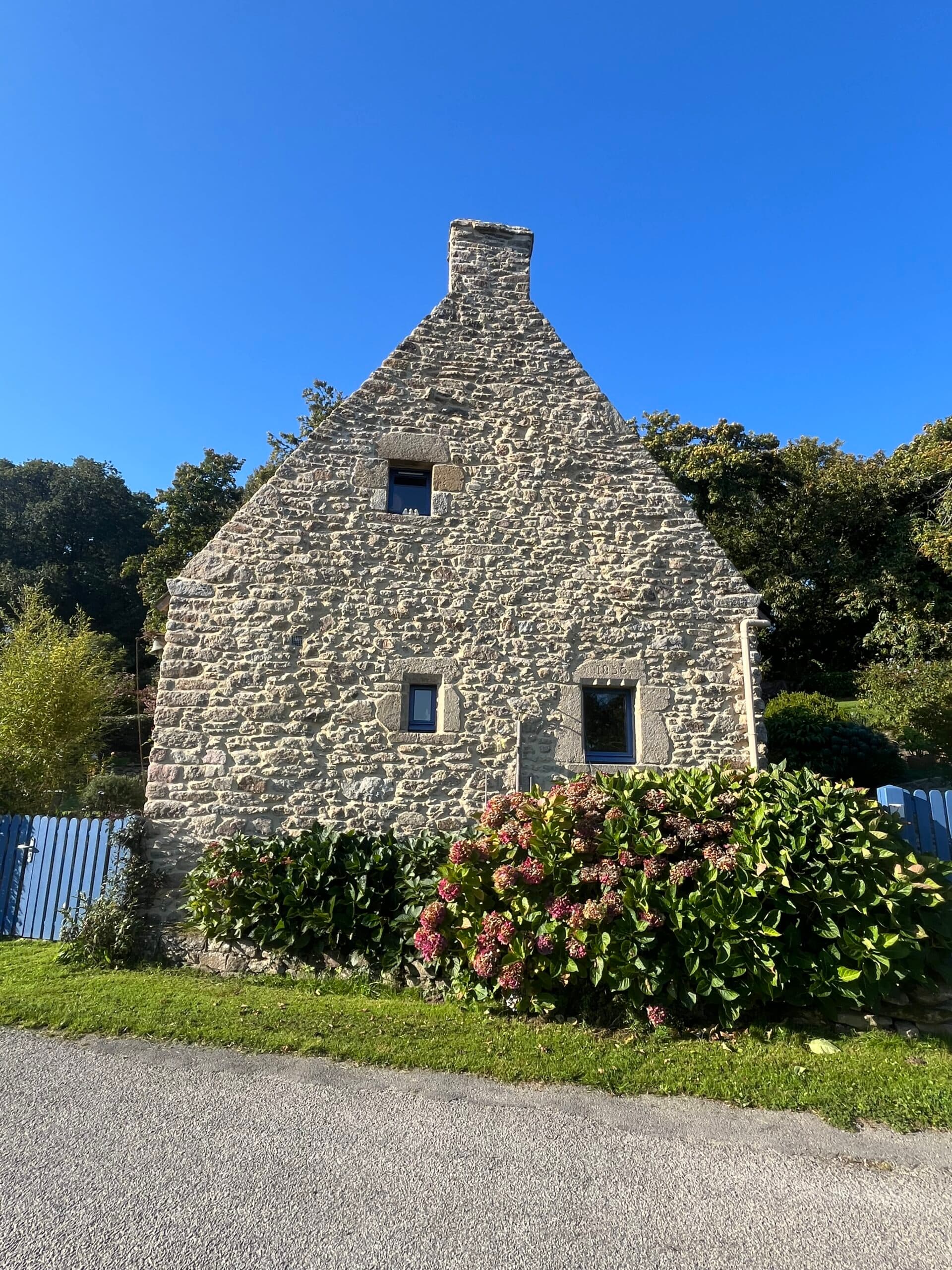 Façade de longère bretonne aux joints de pierre apparente retravaillés, avec jardin paysager.
