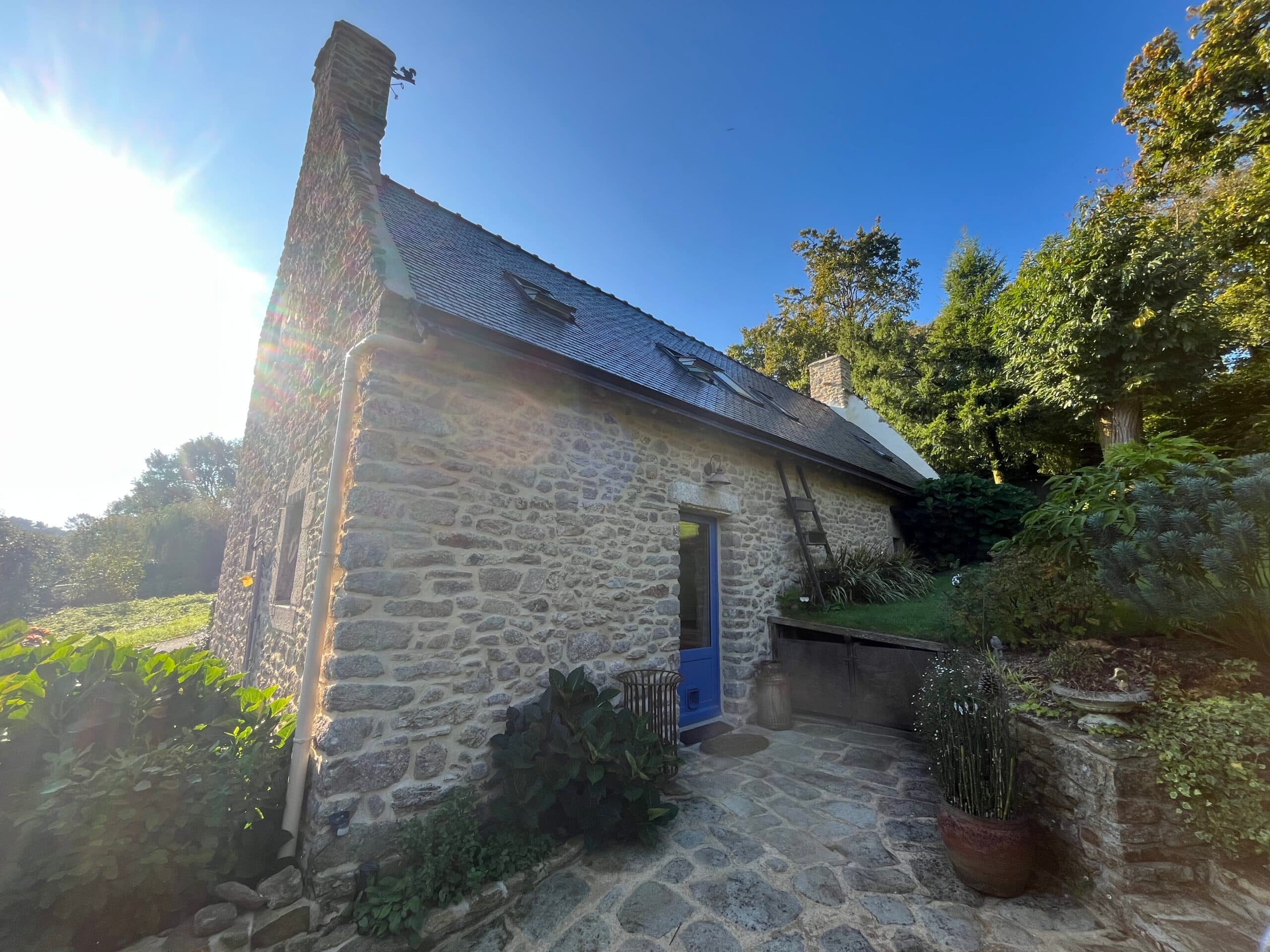 Petite maison bretonne en pierre avec clôture bleue et jardin fleuri, rénovée par AJY Maçonnerie.