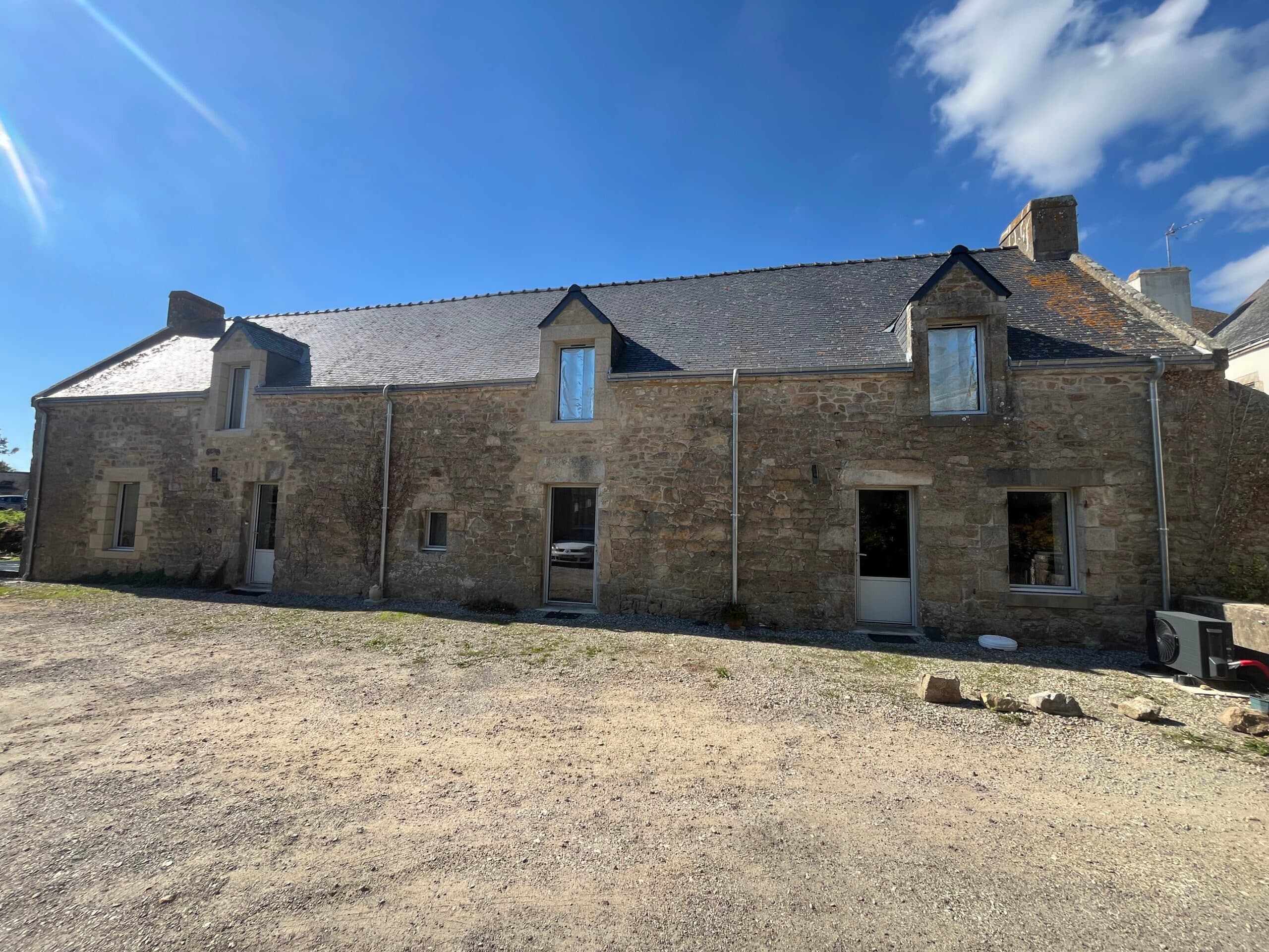 Façade principale d’une longère bretonne restaurée par AJY Maçonnerie avec murs en pierre apparente, encadrements en granit et toiture ardoise.
